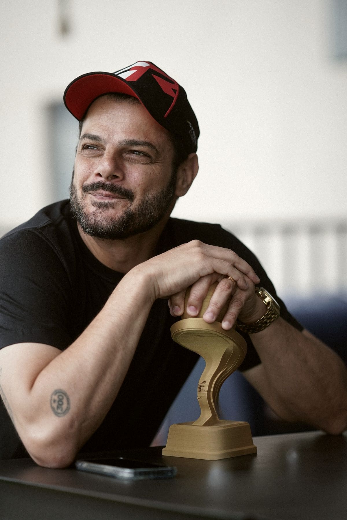 Giuseppe de boné, sorrindo, apoiado num troféu de kart