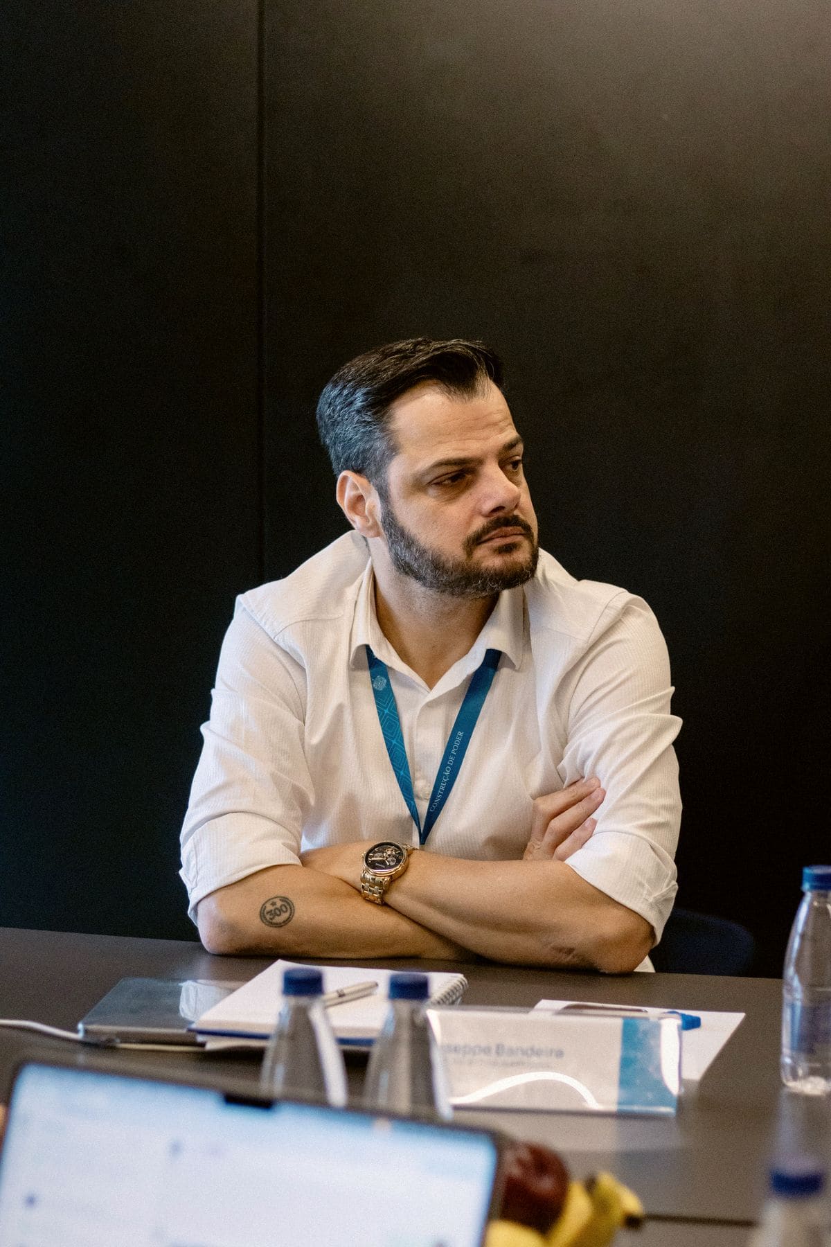 Giuseppe em mesa de debate, de camisa branca, ouvindo