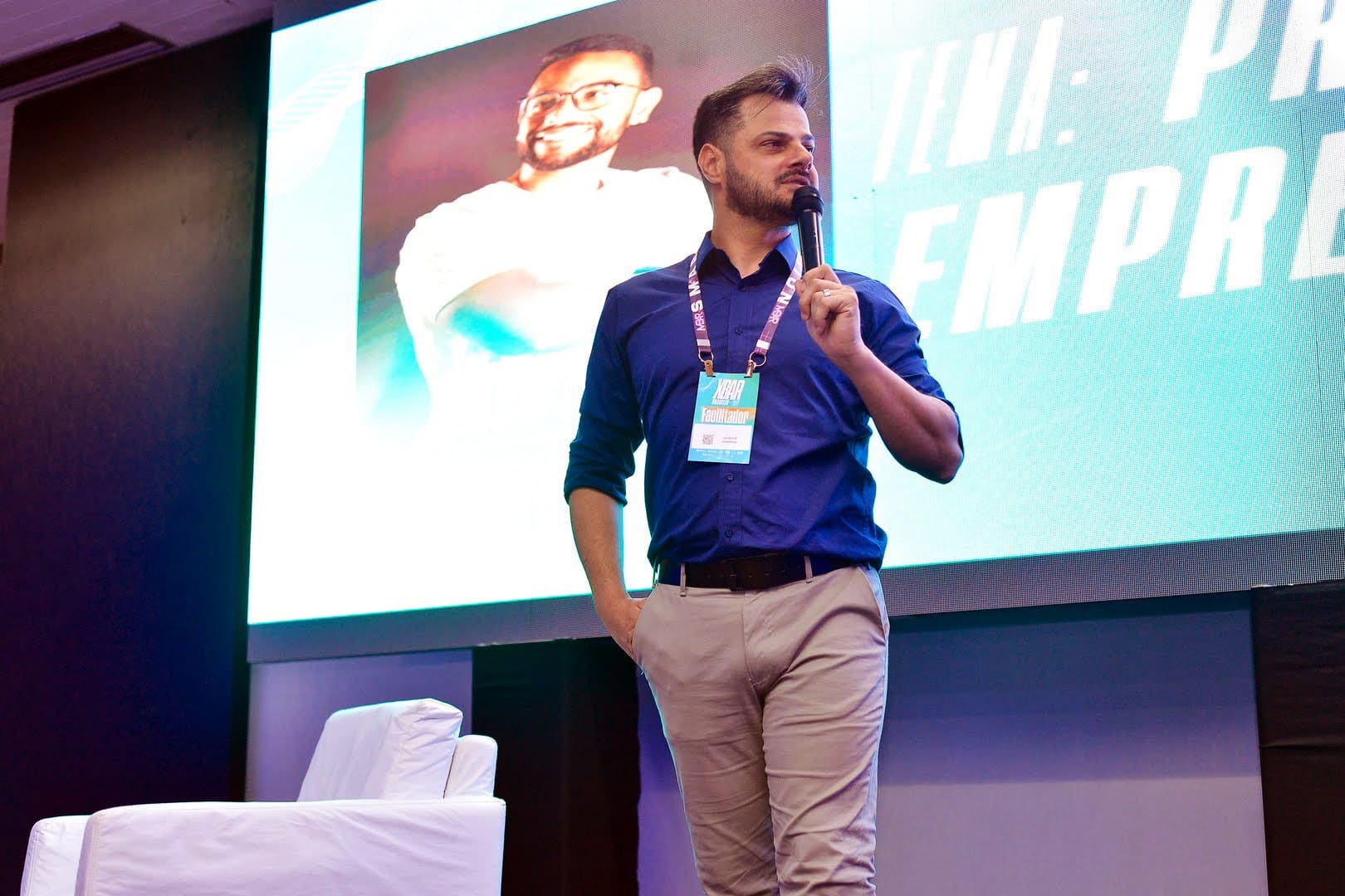 Giuseppe palestrando de camisa azul, com microfone, diante do telão