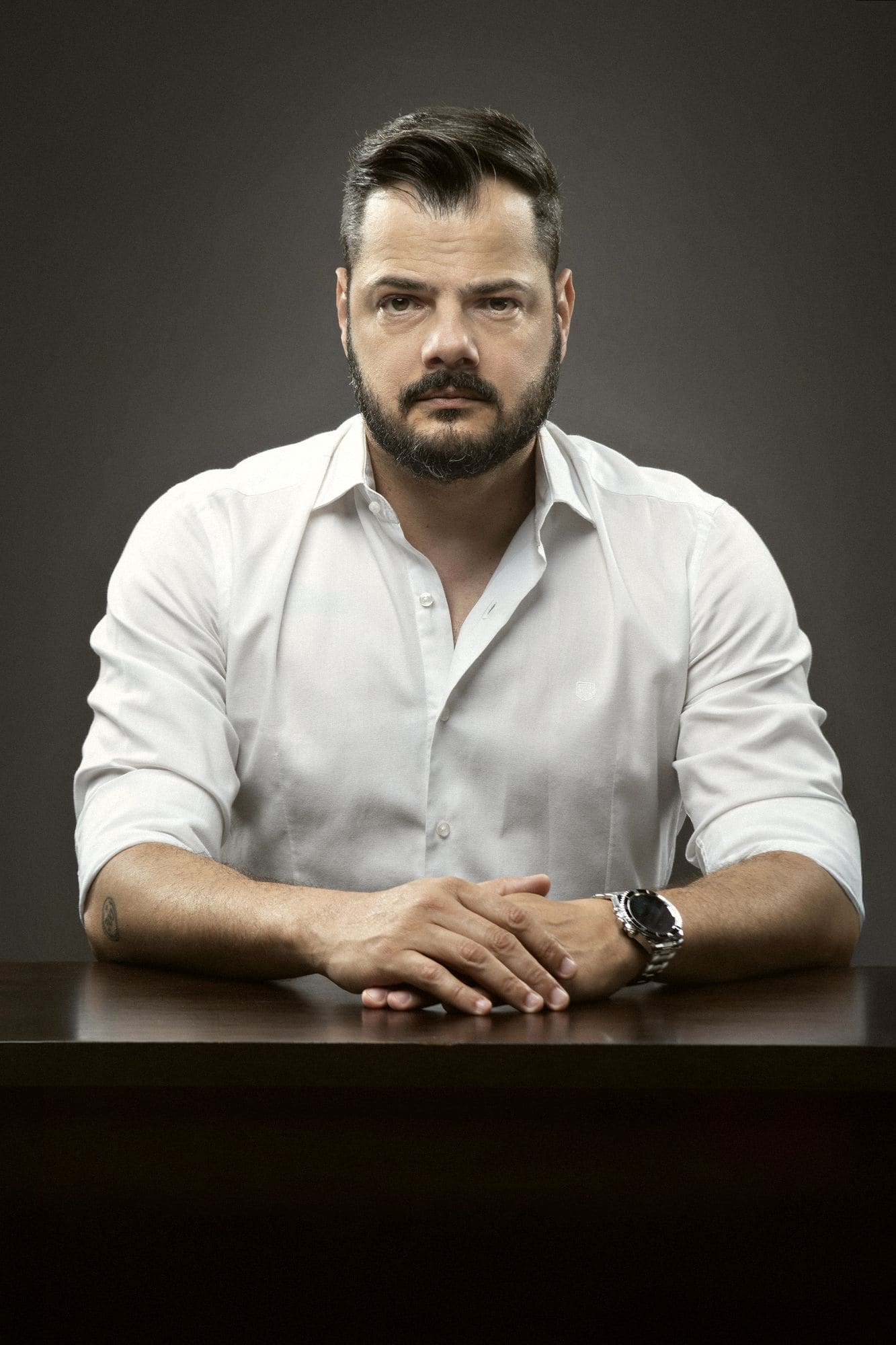 Giuseppe sentado à mesa, de camisa branca, olhando para a câmera